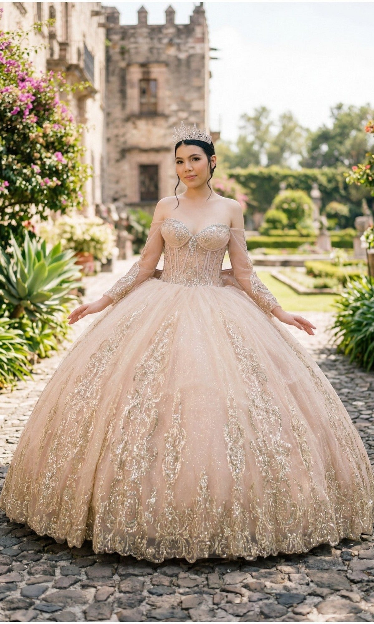 A young woman in the Quinceanera Dress 8545JQ By Cinderella Couture, featuring an off-the-shoulder sweetheart neckline and beaded sequin embellishments, stands on a garden stone path with a historic building in the background.